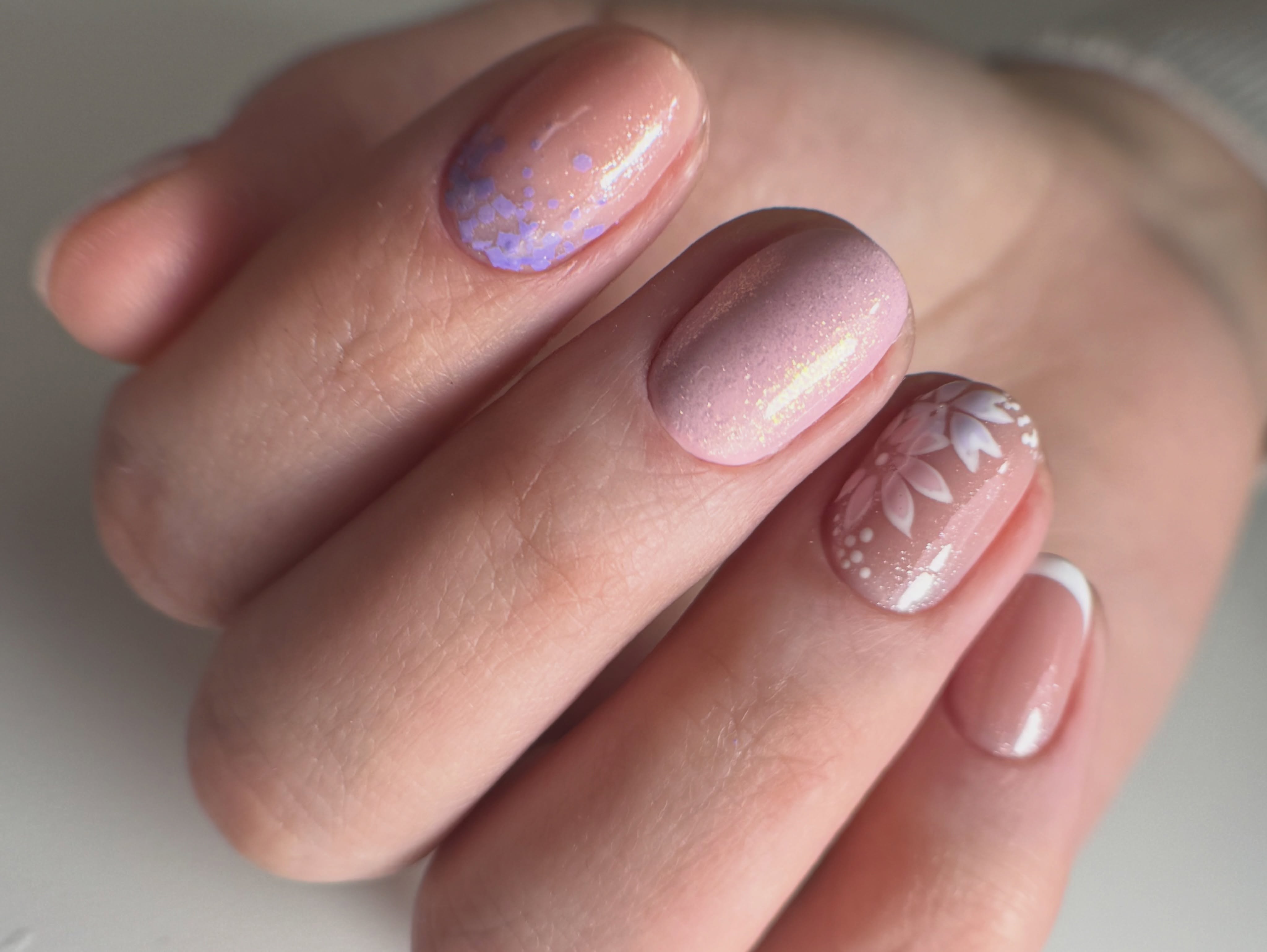 Cuatro uñas rosadas con destellos y una flor blanca pintada